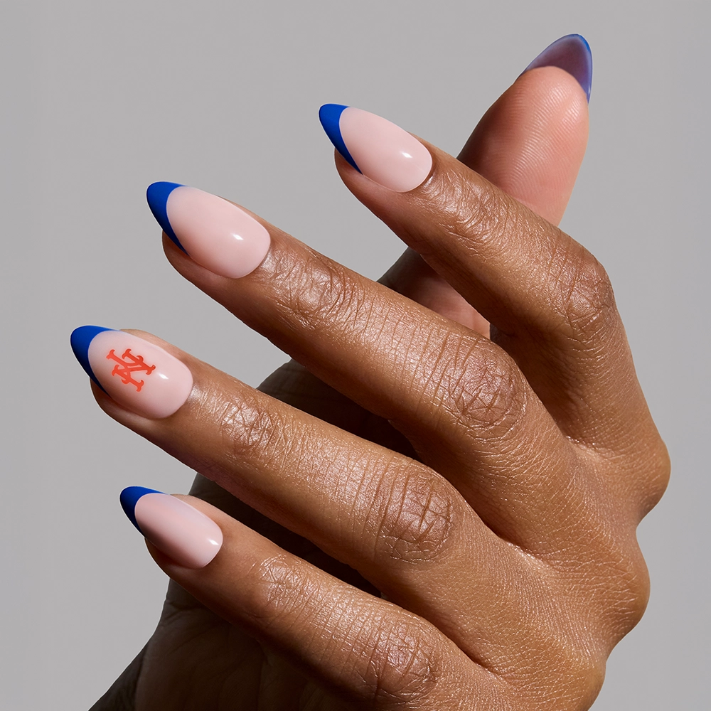 A hand shows almond-shaped nails with a nude base, bright blue French tips, and an orange-accented nail—perfect for fans of the glamnetic New York Mets Press-On Nail Set. - Product image