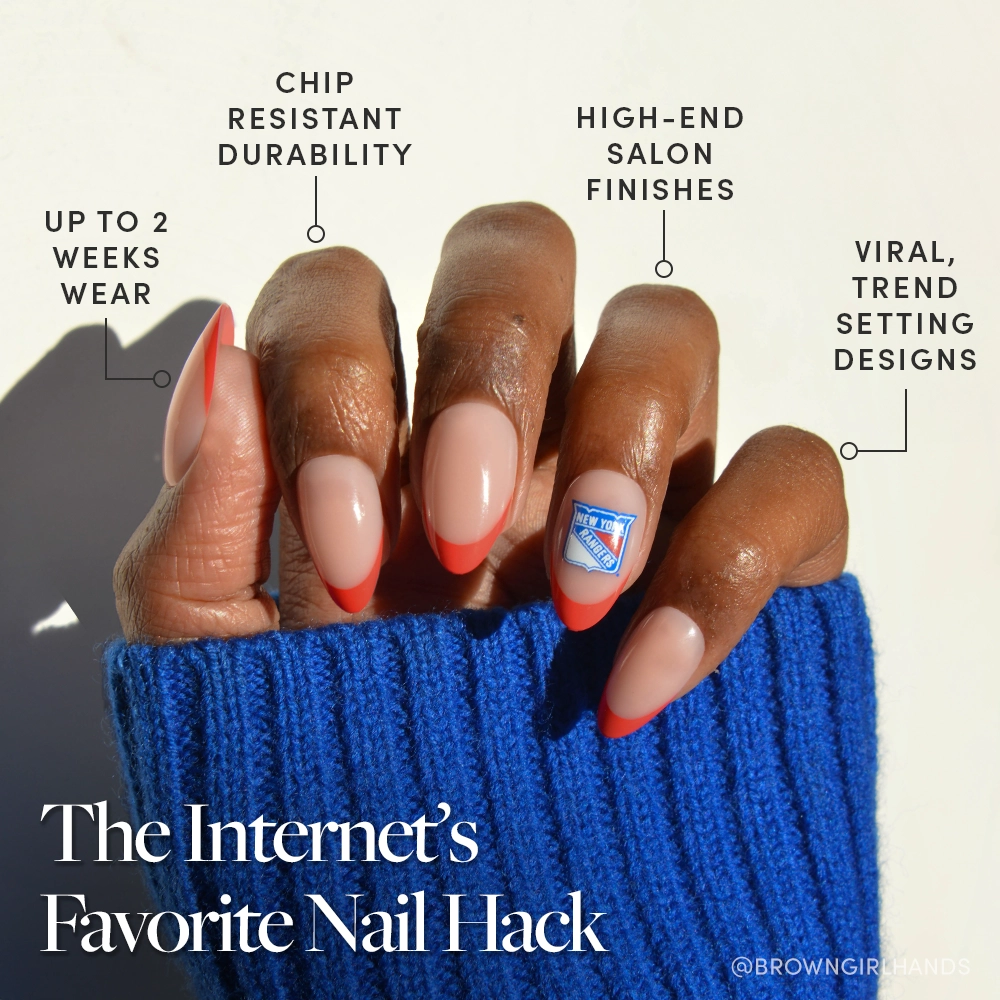 A hand with almond-shaped nude nails featuring bold red New York Rangers French tips and a blue accent nail from the glamnetic New York Rangers Press-On Nail Set, shown with a blue sweater. Overlay text notes durability and trendy designs. - Product image