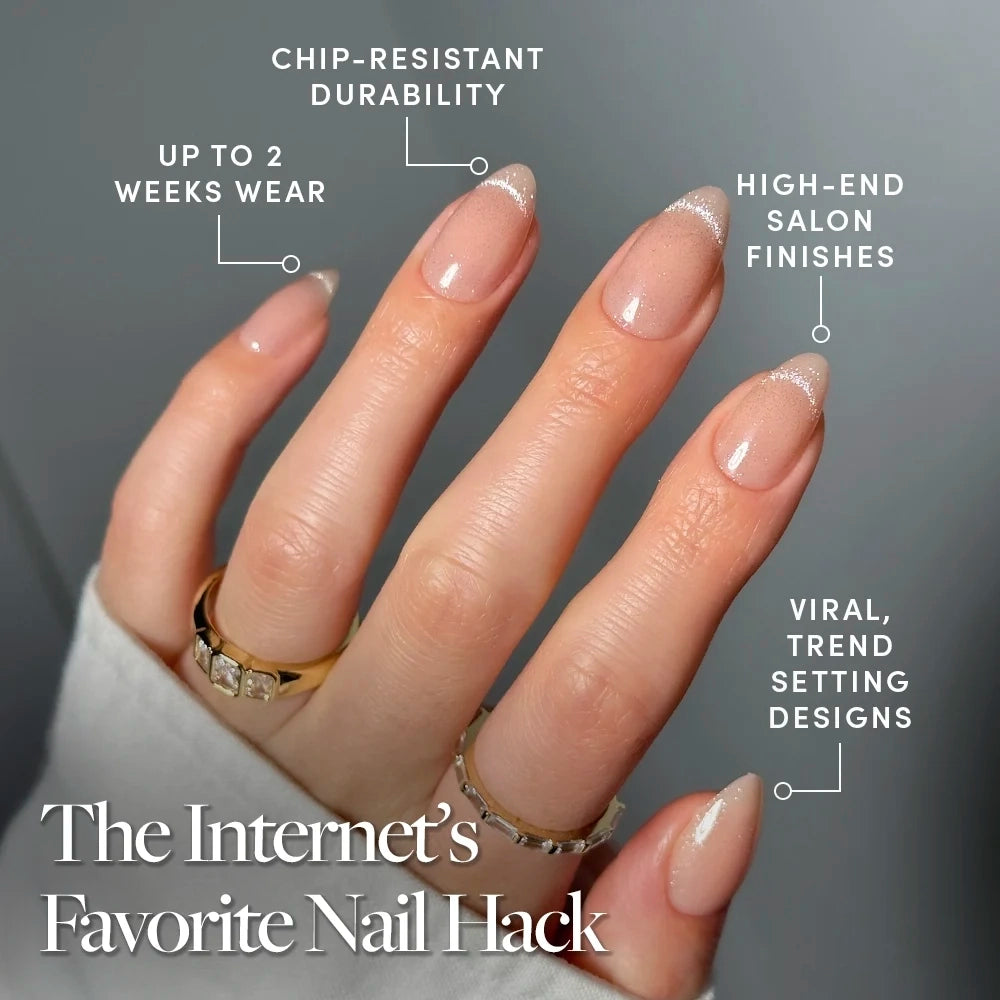 A hand with manicured almond nails showcases the NOT YOUR CINDER-ELLA press-ons from glamnetic, featuring a natural glossy finish with delicate glitter tips. Text highlights their chip-resistant formula, up to two weeks of wear, salon-quality finish, and on-trend design. Complemented by gold rings, these nails let you experience effortlessly beautiful press-ons that deliver a lasting salon look. - Product image