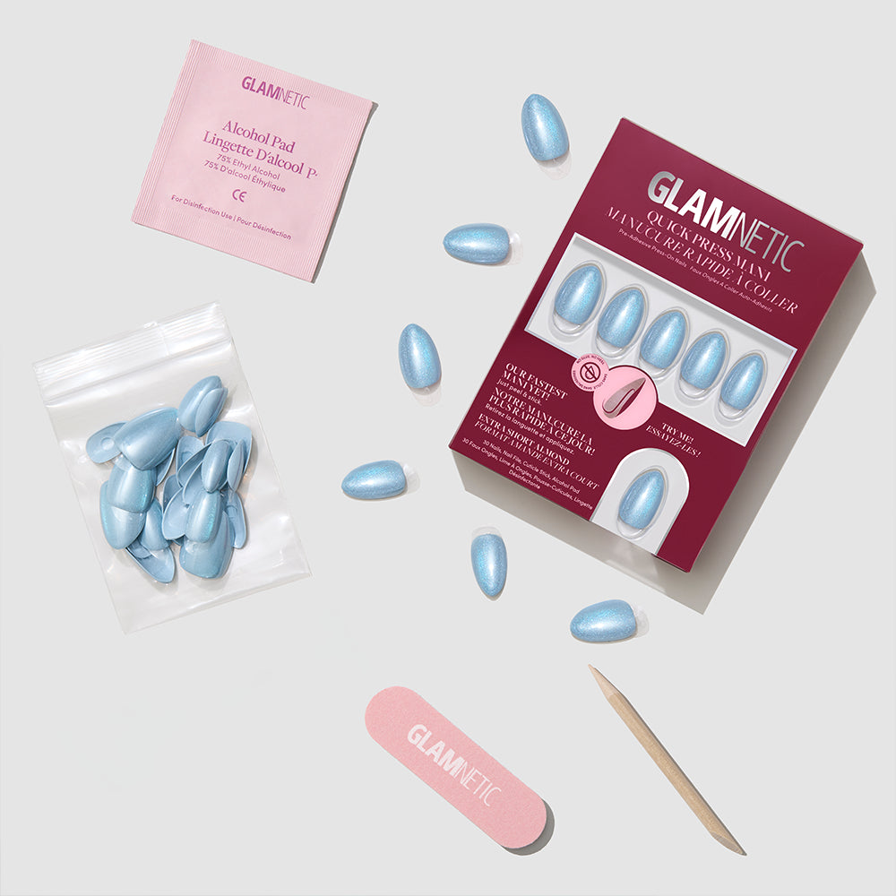 A flat lay of the glamnetic Ocean Prism press-on nail kit, showing blue metallic nails, a nail file, cuticle stick, glue, alcohol pad, and extra nails neatly arranged on a light grey background. - Product image