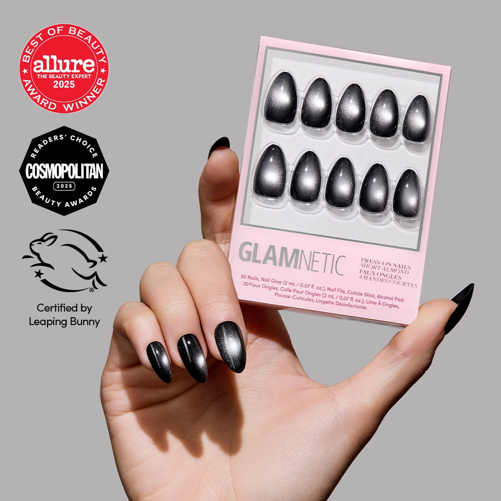 A hand with black, oval-shaped Obsidian press-on nails holds a pink glamnetic box of salon-quality press-ons. The box contains ten black nails, with award and certification logos shown on the left.