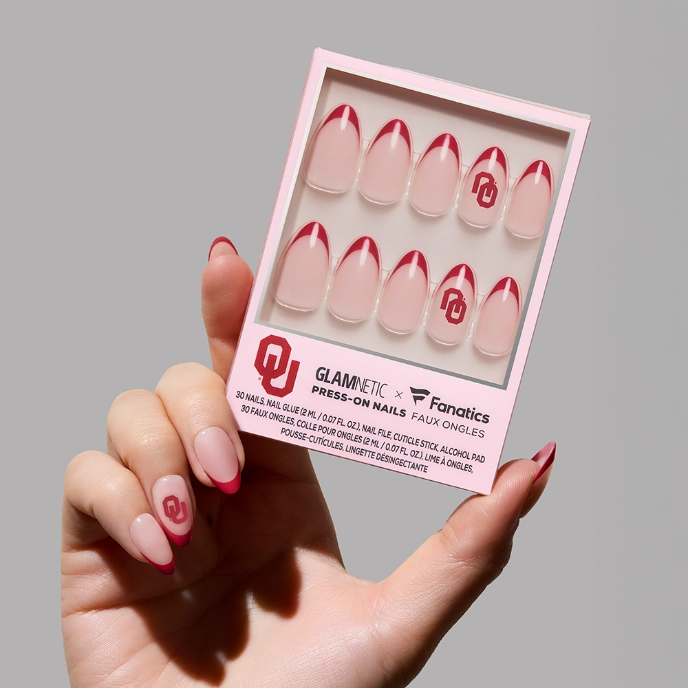 A hand holds the glamnetic Oklahoma Sooners Press-On Nail Set—salon-quality nails with pink bases, red French tips, and the University of Oklahoma logo—in an officially licensed box.