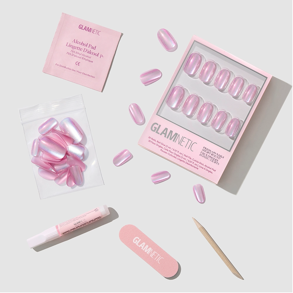 The glamnetic Oyster Glow set includes pink pearlescent, short round press-on nails with nail glue, cuticle stick, mini file, alcohol pad, and extra nails—all displayed on a light gray background.