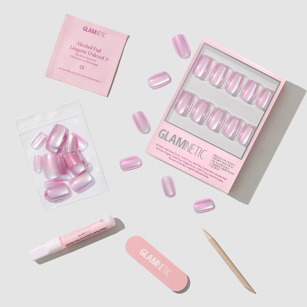 The glamnetic Oyster Shell set includes short squoval pink pearlescent press-on nails, extra nails, nail glue, an alcohol pad, a file, and a cuticle stick—all arranged on a light gray background.