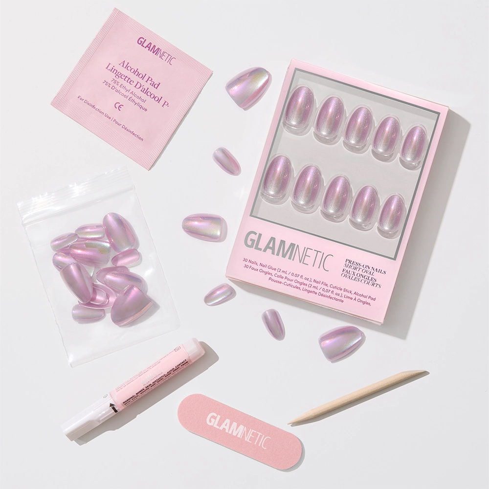 The glamnetic Oyster Press-On Nail Set includes iridescent pink and pearlescent purple nails, a wooden cuticle stick, pink nail file, nail glue, alcohol pad, and extra nails—stylishly displayed on a white surface. - Product image