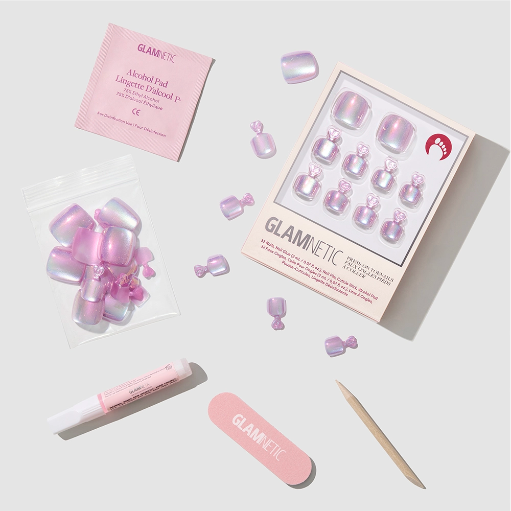 Glamnetic's Oyster Toenail set features iridescent pink, pearlescent press-on nails with application tools—nail file, cuticle stick, nail glue, alcohol pad, and extra nails—all neatly displayed on a light gray background. - Product image