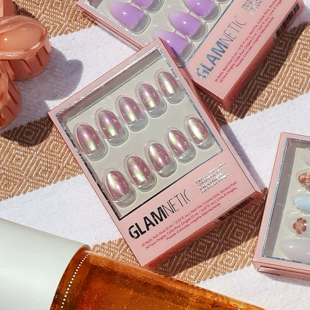 Glamnetic Oyster press-on nails with a pearlescent purple velvet finish are displayed on a striped towel, alongside other nail sets and a yellow-orange bottle. - Product image