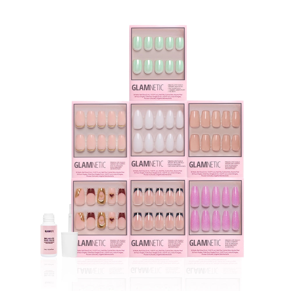 Seven boxes of glamnetic Main Stage Moment press-on nails are stacked in a pyramid, showcasing salon-quality styles in assorted colors and designs. A nail glue bottle and file are placed in front against a white background. - Product image