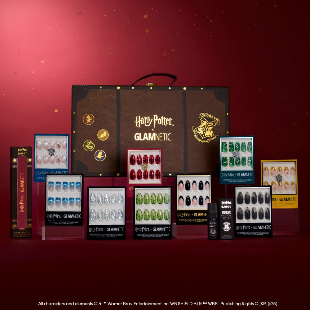 The Harry Potter™ x Glamnetic PR Box by glamnetic features collector’s press-on nails and accessories, displayed before a brown Hogwarts-themed suitcase on a red backdrop, with each set offering unique nail designs inspired by the series.