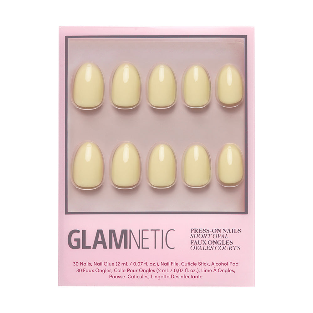 A package of glamnetic Pastel Yellow nail set features 10 short oval, solid pale yellow salon-quality nails with a glossy finish, displayed on a pink backing and visible through a clear window.