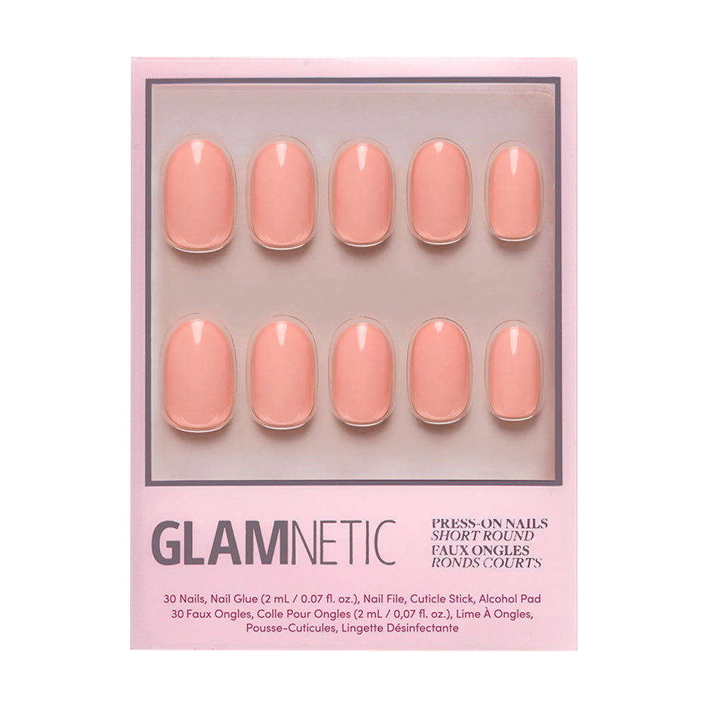 A box of glamnetic Peach Coral reusable nails features a short, round shape in pastel peach, arranged in two rows. The light pink packaging displays product details below the nails.