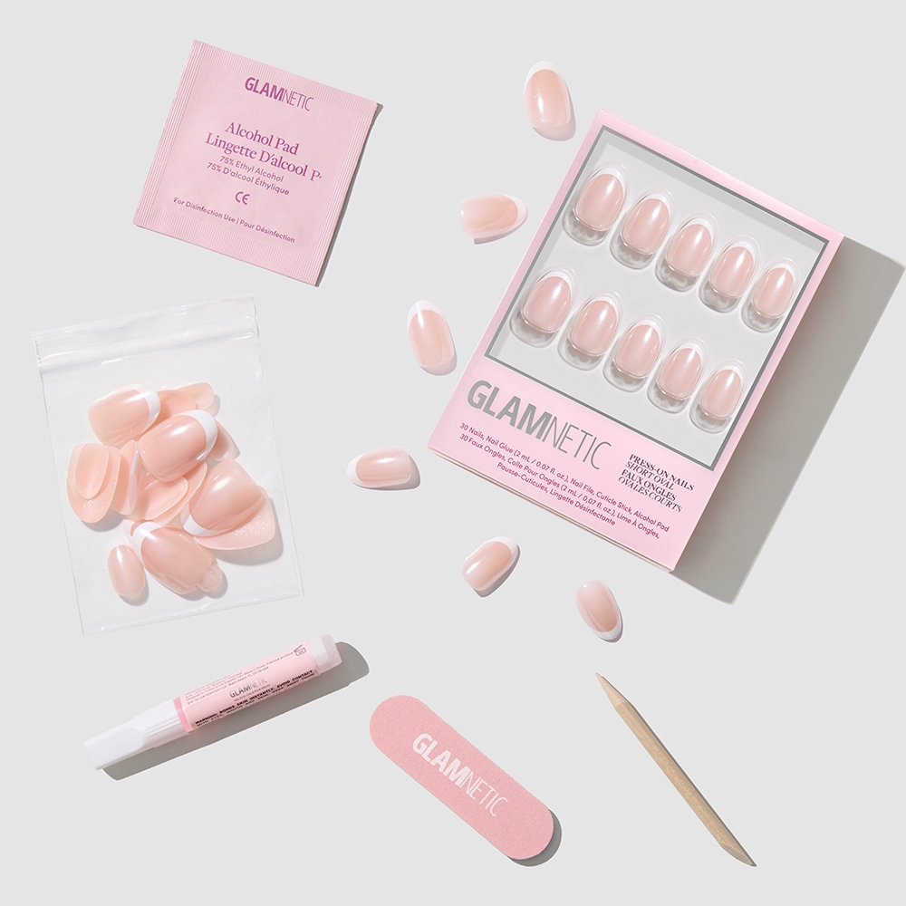The glamnetic Pearlfect set features pink pearlescent press-on nails, a nail file, cuticle stick, glue, alcohol pad, and extra nails—all arranged neatly on a light gray background. - Product image