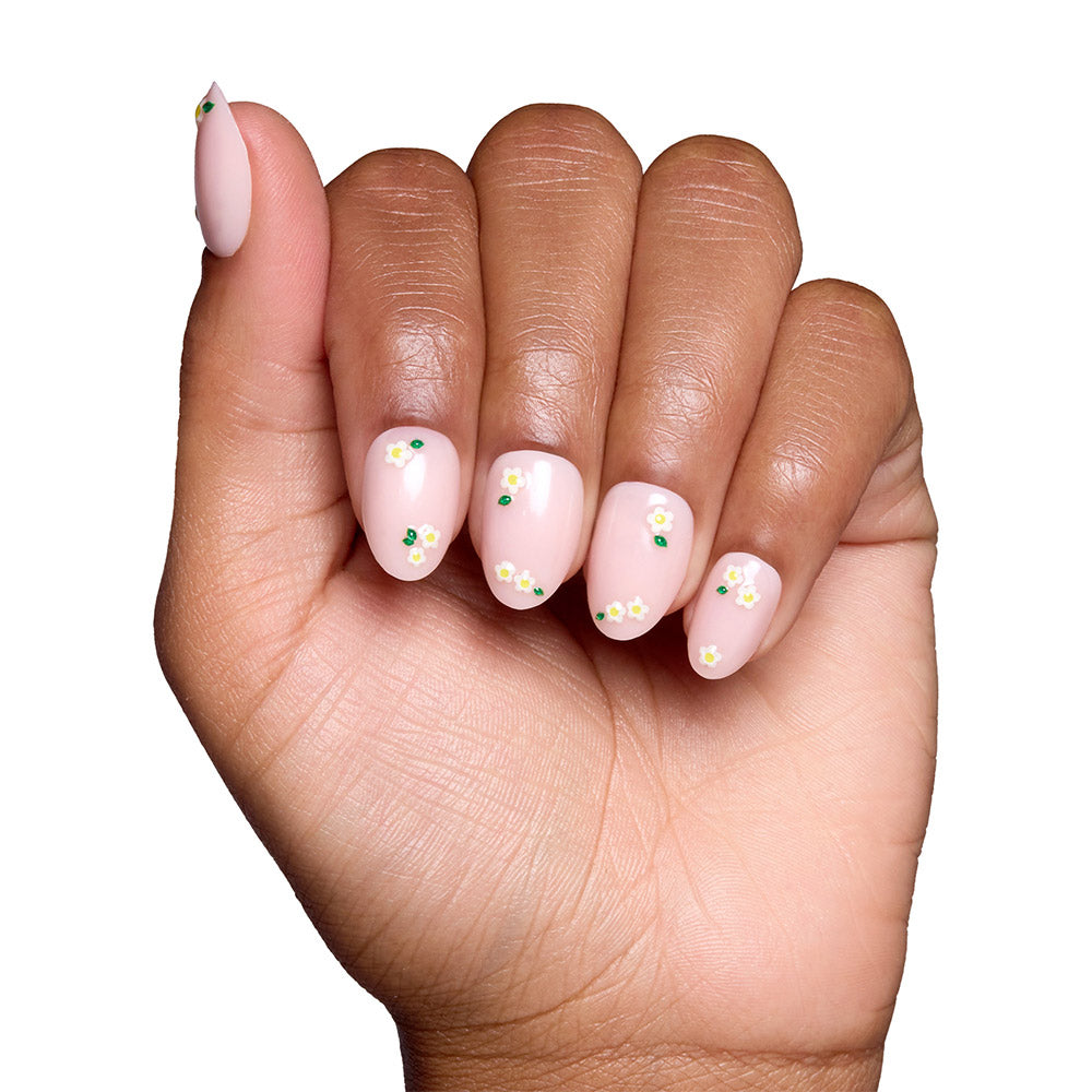 A hand features Petals by glamnetic: light pink, short oval nails with glossy finish and delicate white and yellow daisy accents on each fingernail, shown against a white background. - Product image