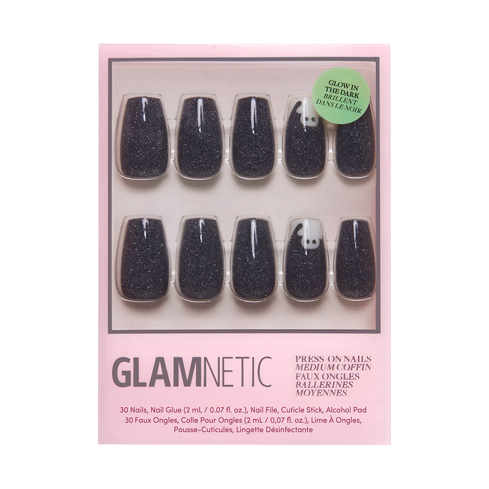 Introducing the glamnetic Phantom Glow Nail Set: a box of chic coffin-shaped, glow-in-the-dark press-on nails in black glitter, with one nail featuring a white ghost design. The set comes complete with nail glue and accessories, and packaging includes a sticker highlighting their glow-in-the-dark effect.