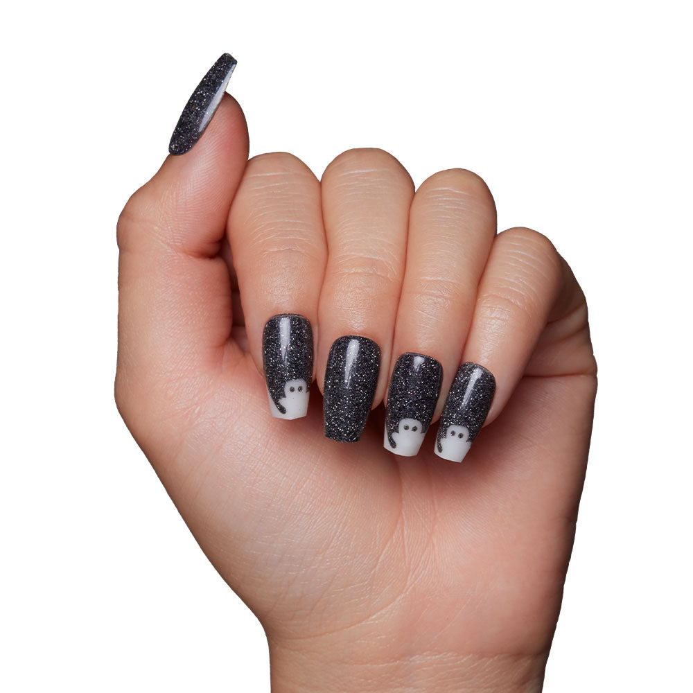 A hand adorned with long, black, glittery coffin-shaped nails from glamnetic’s Phantom Glow set features small white ghost designs on four fingernails, shown against a white background—a hauntingly chic look. - Product image