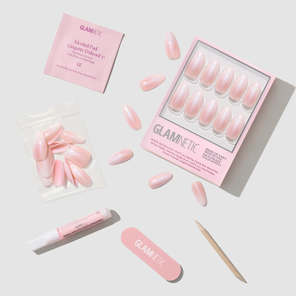 A flat lay of glamnetic’s Pink Pearl kit displays ombre French tip press-on nails, a nail file, cuticle stick, adhesive tube, alcohol pad, and extra nails neatly arranged on a light background. - Product image
