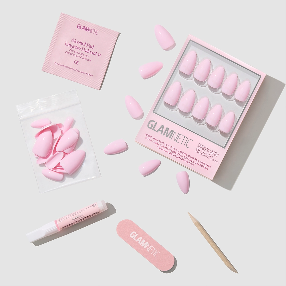 The Pink Poise set by glamnetic includes extra short almond blush pink press-on nails, nail glue, a wooden cuticle stick, a pink nail file, and an alcohol pad—all displayed on a white background.