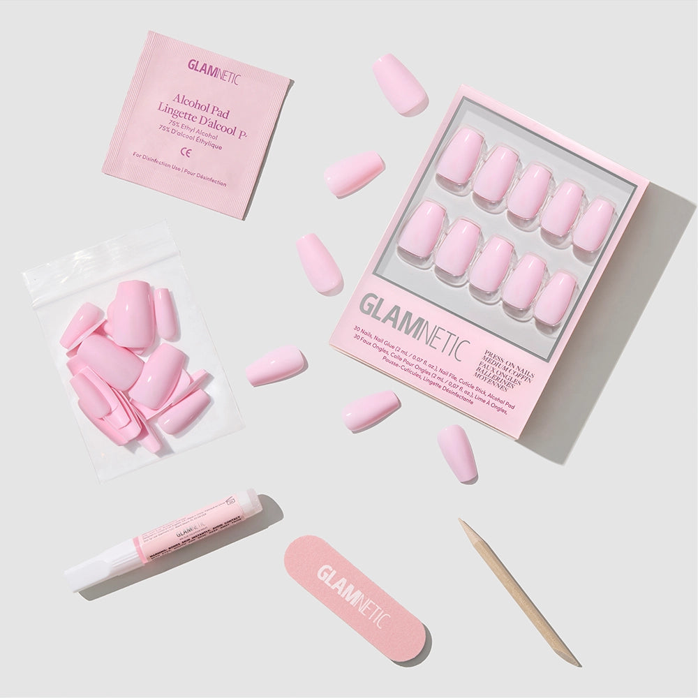 The Pink Statement by glamnetic features glossy blush medium coffin nails with accessories—alcohol pad, glue tube, mini file, cuticle stick, and extra nails—neatly arranged on a light gray background.