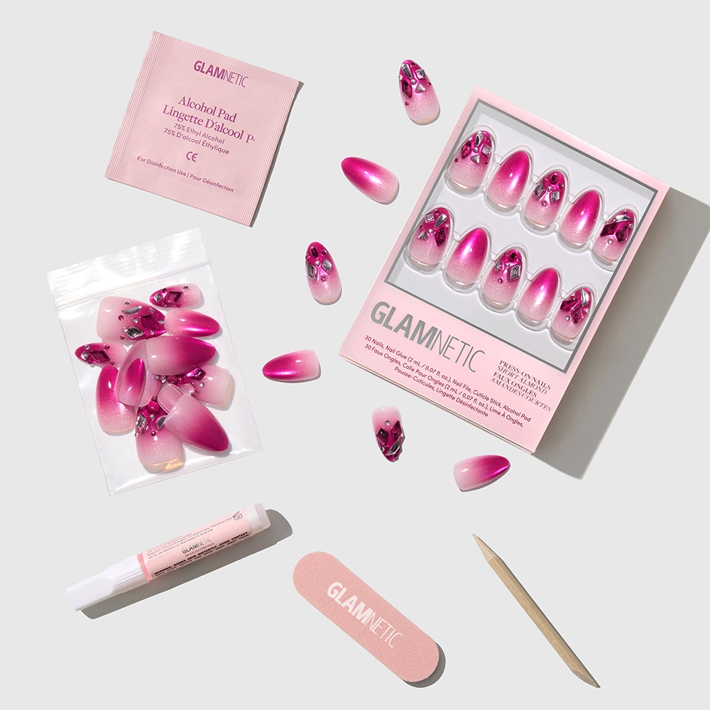A flat lay of glamnetic's Pink Tourmaline manicure set, featuring floral and ombre pink extra short almond press-on nails, nail glue, alcohol pad, nail file, cuticle stick, and a small pouch. - Product image