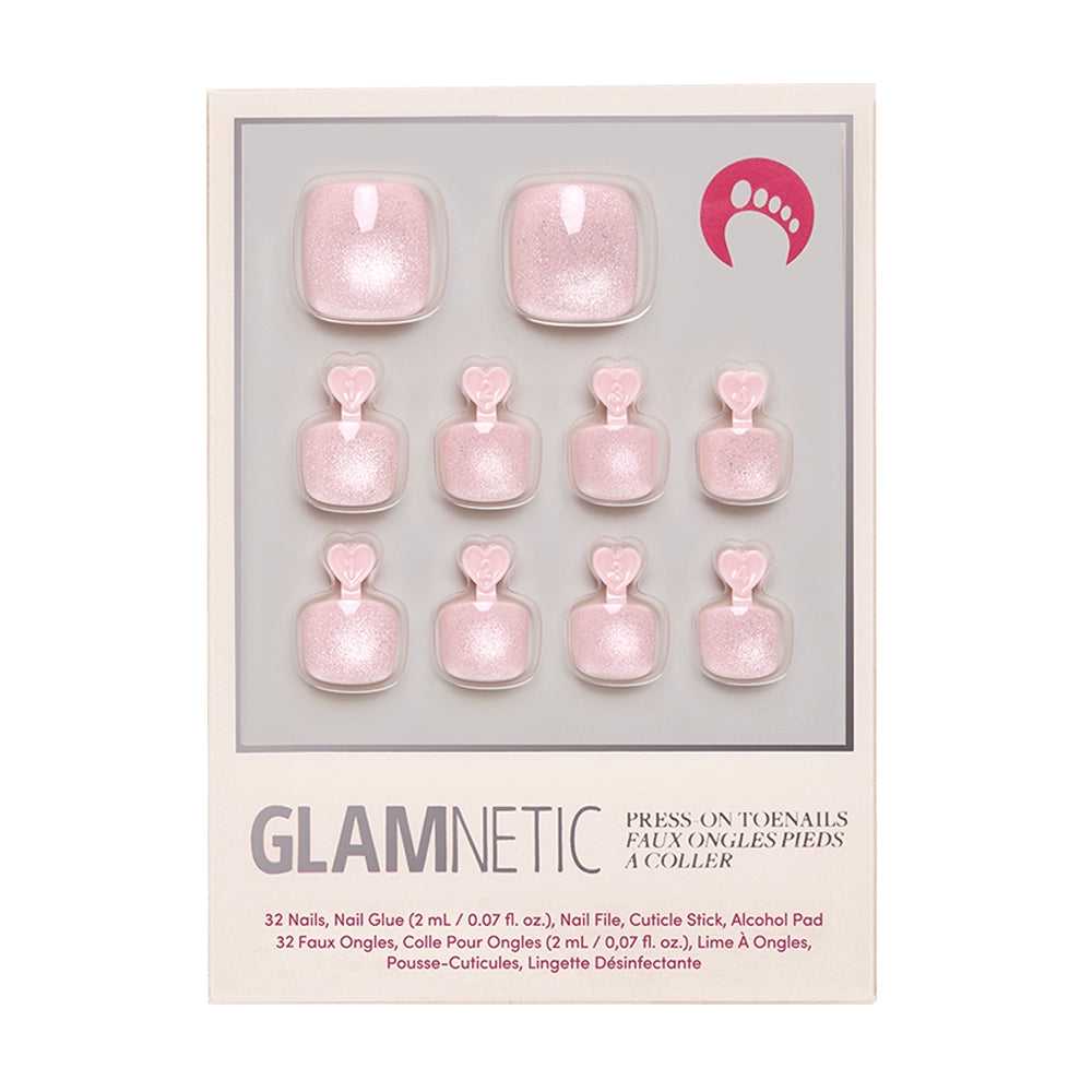The glamnetic Pinky Promise Toenail set features shimmery pale pink vegan press-on toenails with heart-shaped tabs, arranged in two rows. The package includes nail glue, file, cuticle stick, and an alcohol pad.