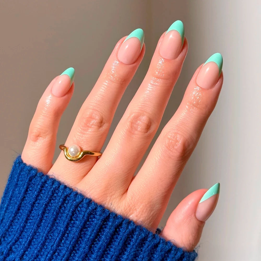 Short almond nails in Pistachio Crème by glamnetic with a sheer nude base and light green French tips, worn with a gold ring featuring a small pearl.