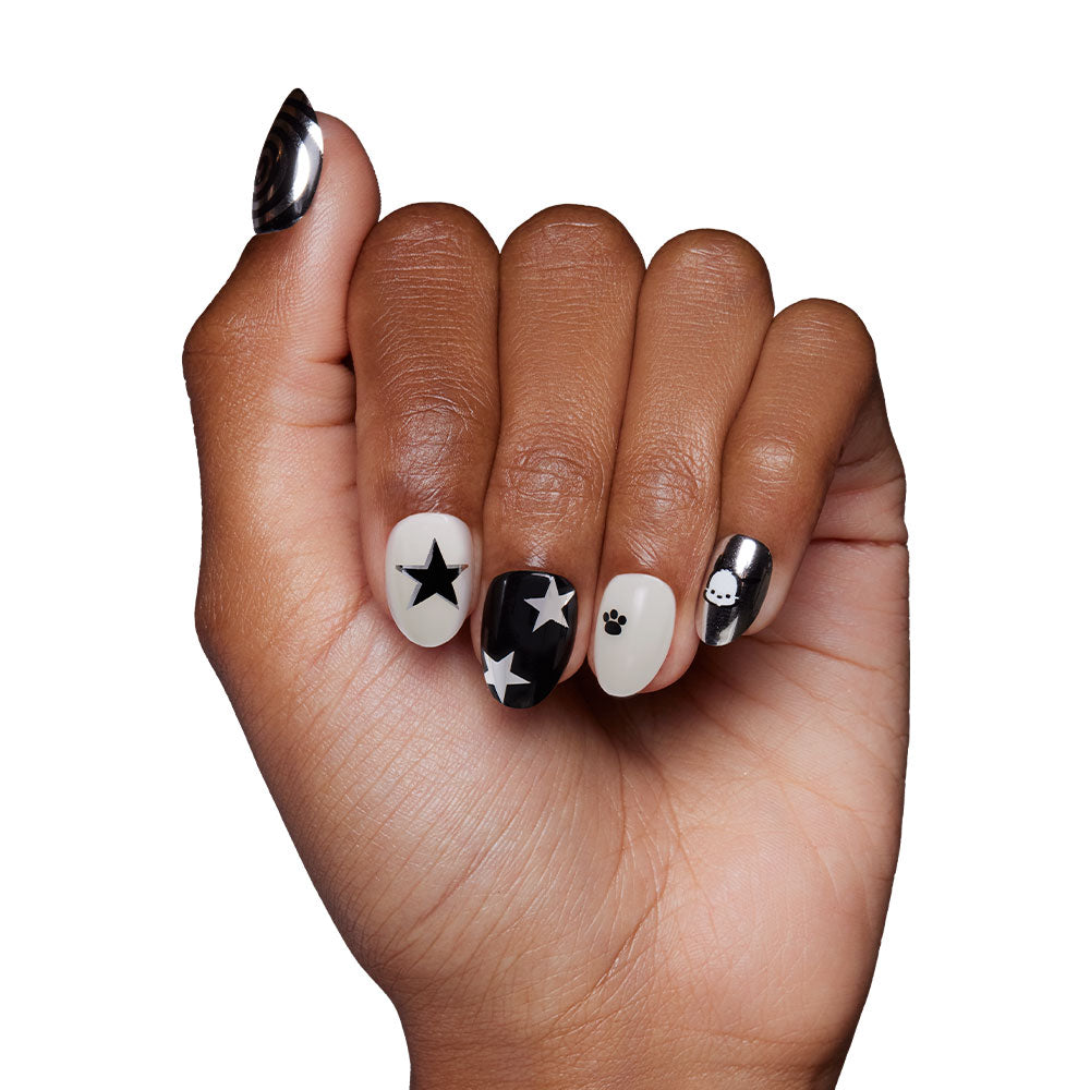 A hand with medium skin tone displays black and white nails featuring stars, a skull, and geometric designs created with the Pochacco™ press-on nail set, styled in collaboration with Sanrio, shown against a white background. - Product image