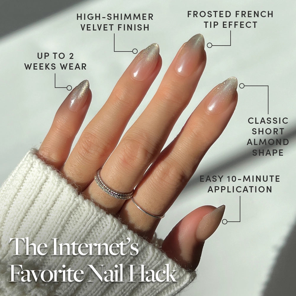 A hand adorned with shimmering short almond nails featuring a frosted French tip from glamnetic’s Polar Night set, styled with rings and a cozy white sweater. The text highlights the easy press-on application in just 10 minutes, up to 2 weeks of wear, and standout features of these salon-quality glamnetic nails. - Product image