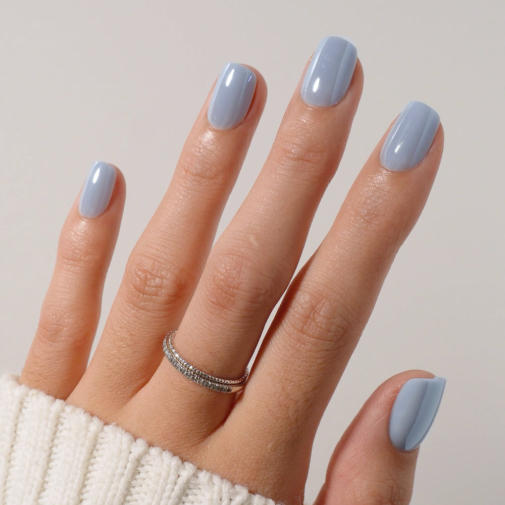 A hand with nails manicured in glamnetic’s Powder Bleu—a light blue shade with a subtle glazed finish—wears a silver ring adorned with small stones and rests on a white ribbed sweater. - Product image