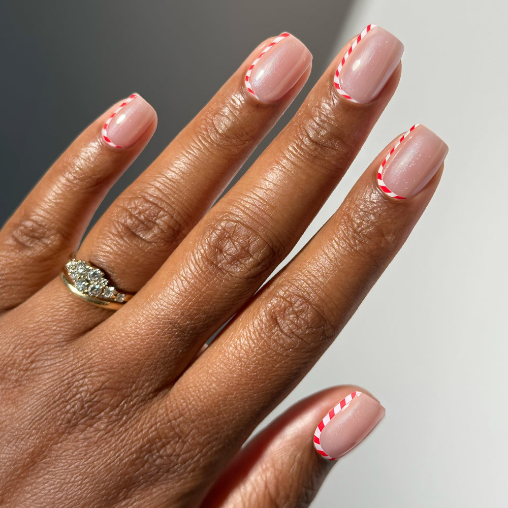 Short, manicured Pretty in Peppermint holiday nails with a sheer nude base and a candy cane-inspired red and white striped tip.
