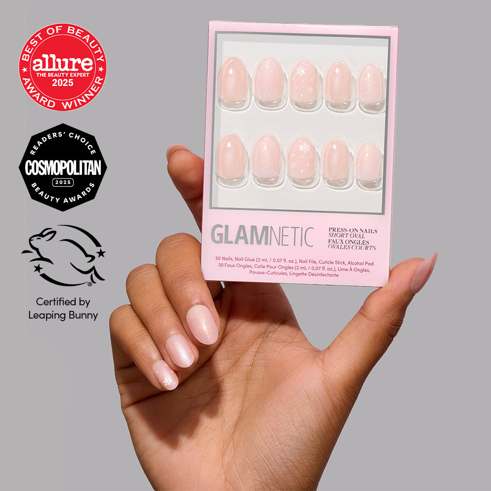A hand displays short, oval Glamnetic Prosecco Pearl press-on nails next to packaging featuring Allure and Cosmopolitan award seals and a Leaping Bunny certification logo. - Product image