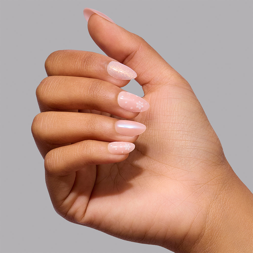 Hand wearing almond-shaped Glamnetic Prosecco Pearl press-on nails in iridescent light pink, featuring white snowflake and dot patterns on two nails. - Product image