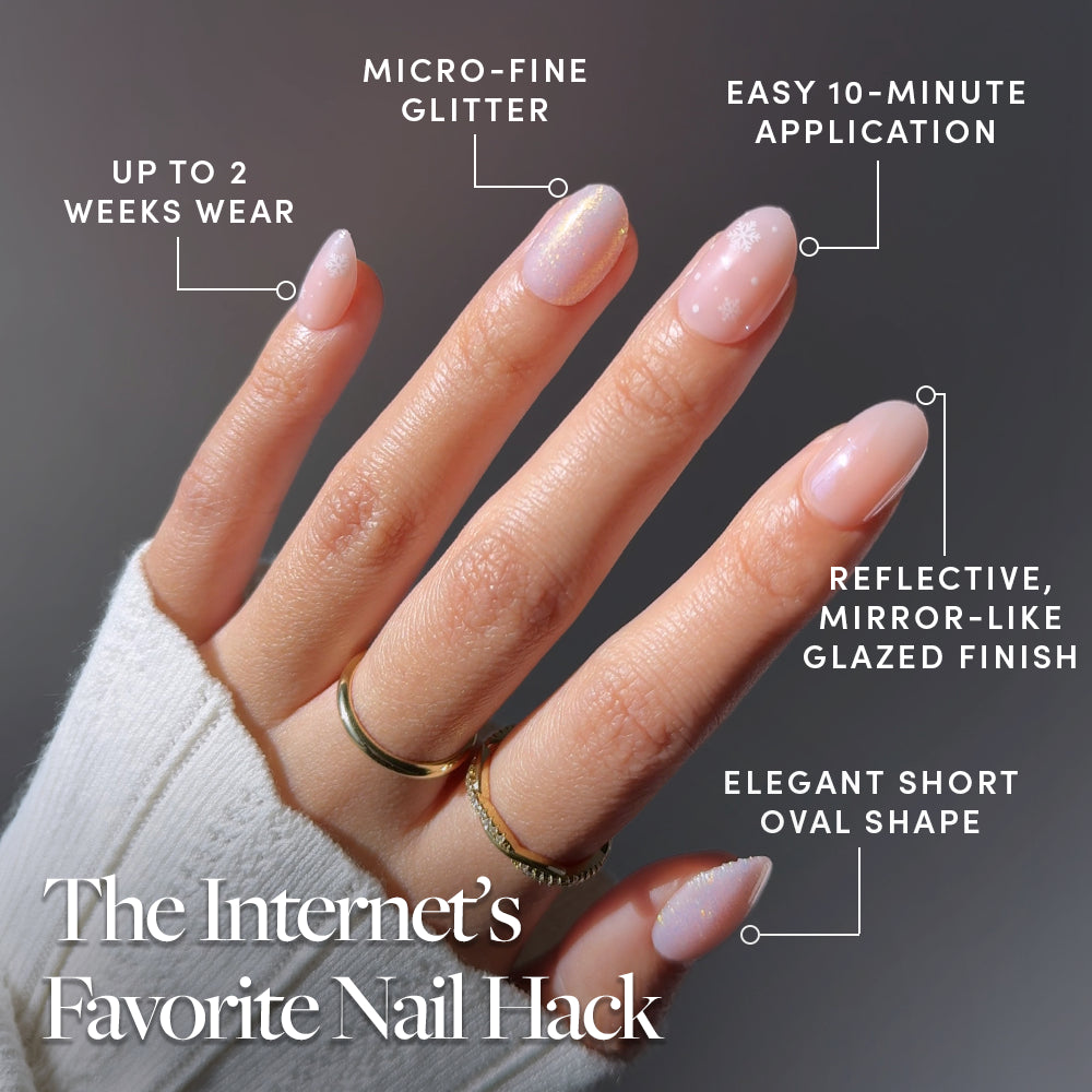 Hand with short oval Glamnetic Prosecco Pearl press-on nails featuring a glittery, glazed finish and a small snowflake design, with text callouts highlighting features like two-week wear, easy application, and a mirror-like finish. - Product image
