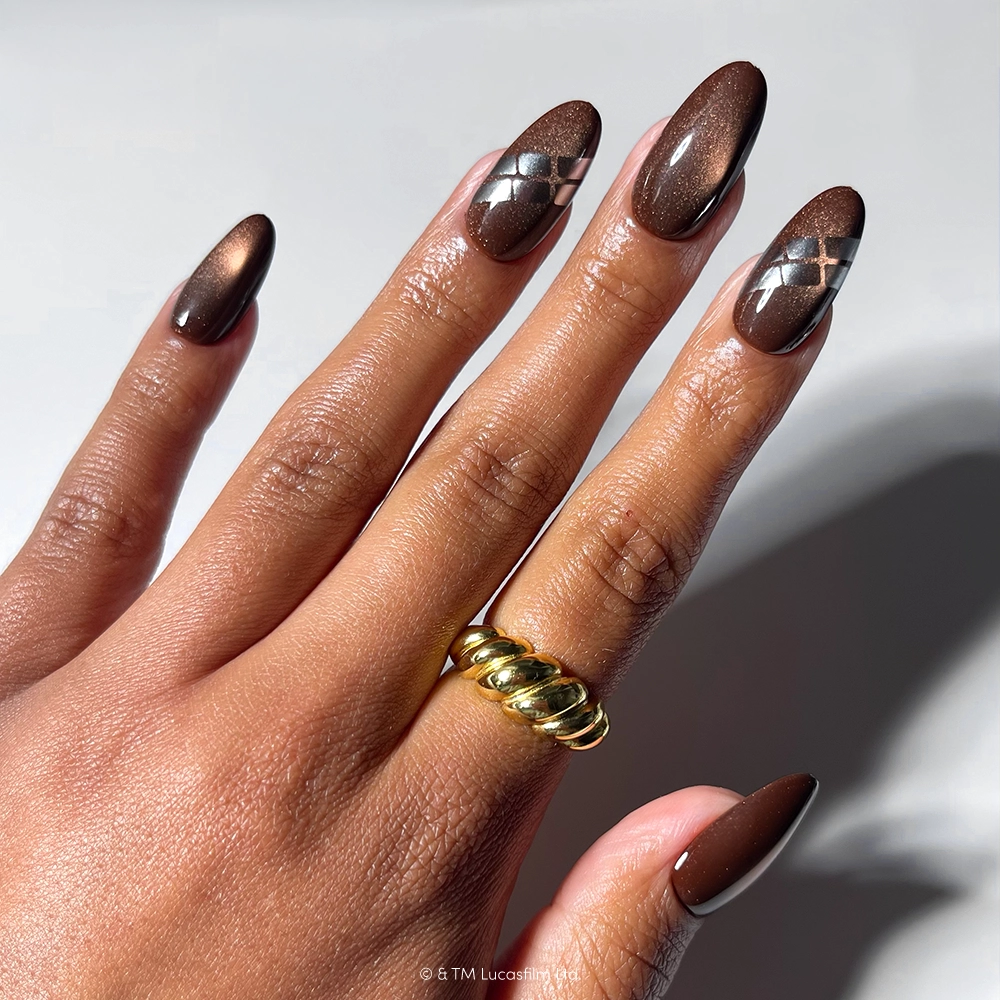A hand with long, brown, almond-shaped nails featuring a diamond pattern on two nails. The person is wearing a thick, twisted gold ring on their middle finger. This unique look showcases the “Punch It, Chewie” nail set by glamnetic—a perfect choice for fans seeking stylish, vegan and cruelty-free nails. - Product image