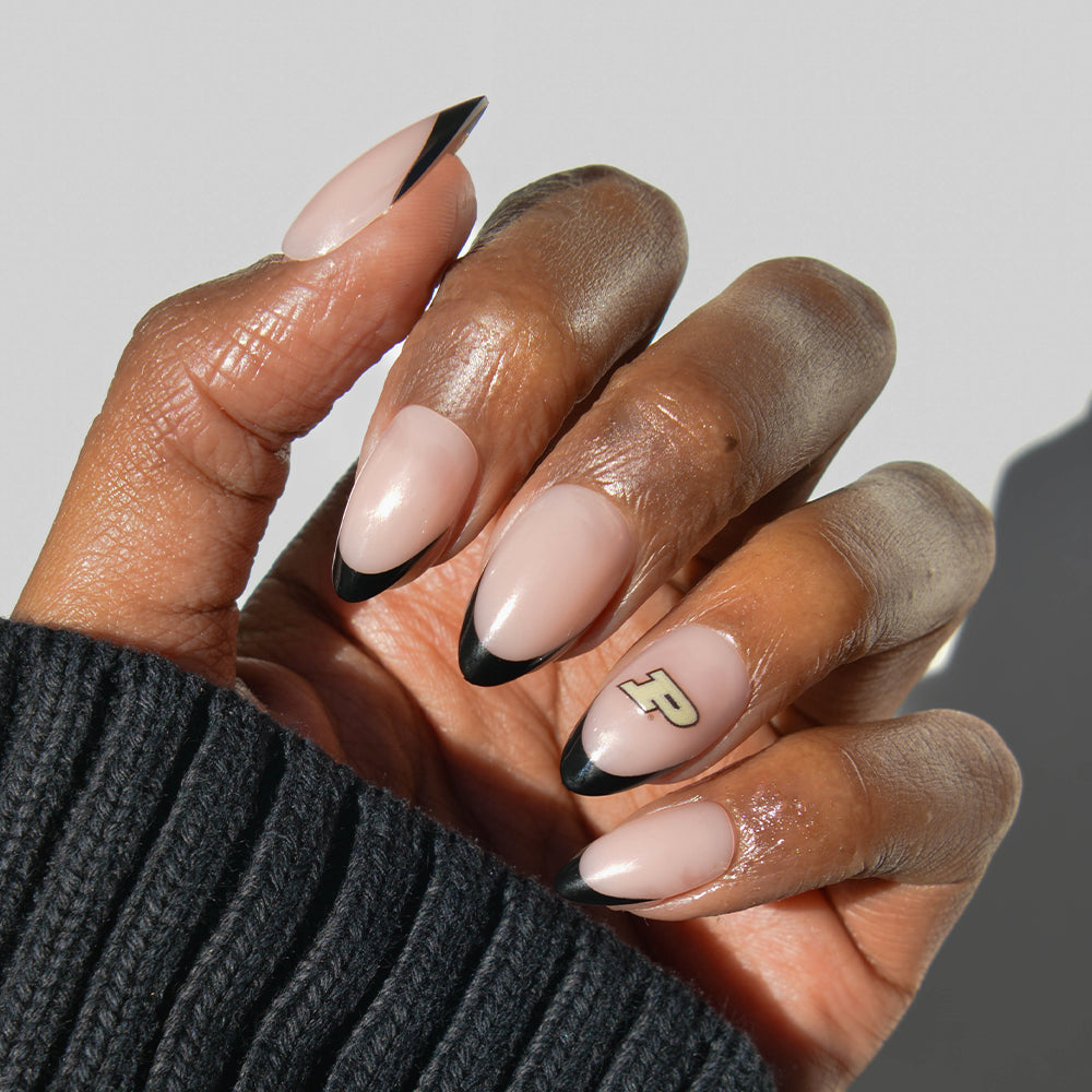 A hand wears glamnetic Collegiate Press-On Nails with almond-shaped black French tips and a gold “P” decal accenting the ring finger, paired with a black ribbed sweater. - Product image