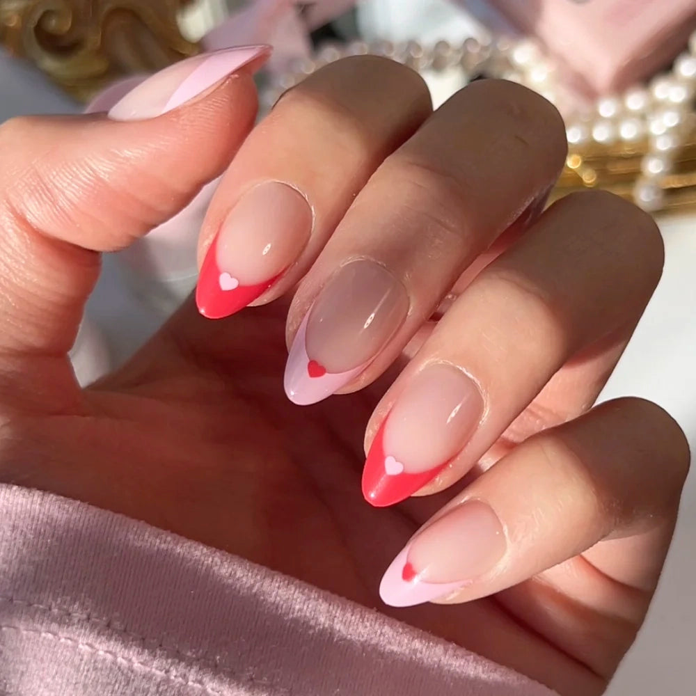 Short almond Pure Hearted press-on nails by glamnetic featuring a pink and red French tip manicure, each with a small heart at the base of the tip.