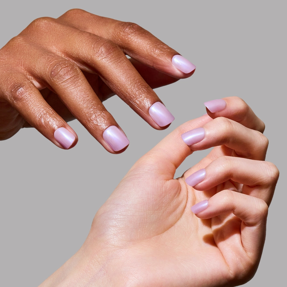 Two hands, one with a darker skin tone and one lighter, showcase glamnetic's Purple Pixie manicure in pastel lavender against a plain grey background. - Product image