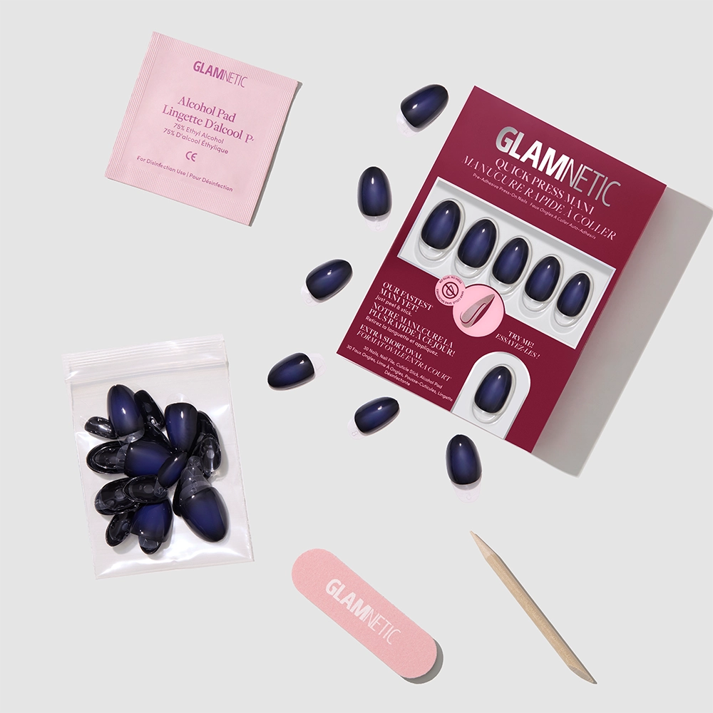 A set of glamnetic Purple Reign press-on nails, along with nail glue, an alcohol pad, a nail file, a cuticle stick, and extra stick-on nails, are arranged neatly on a light gray surface. - Product image