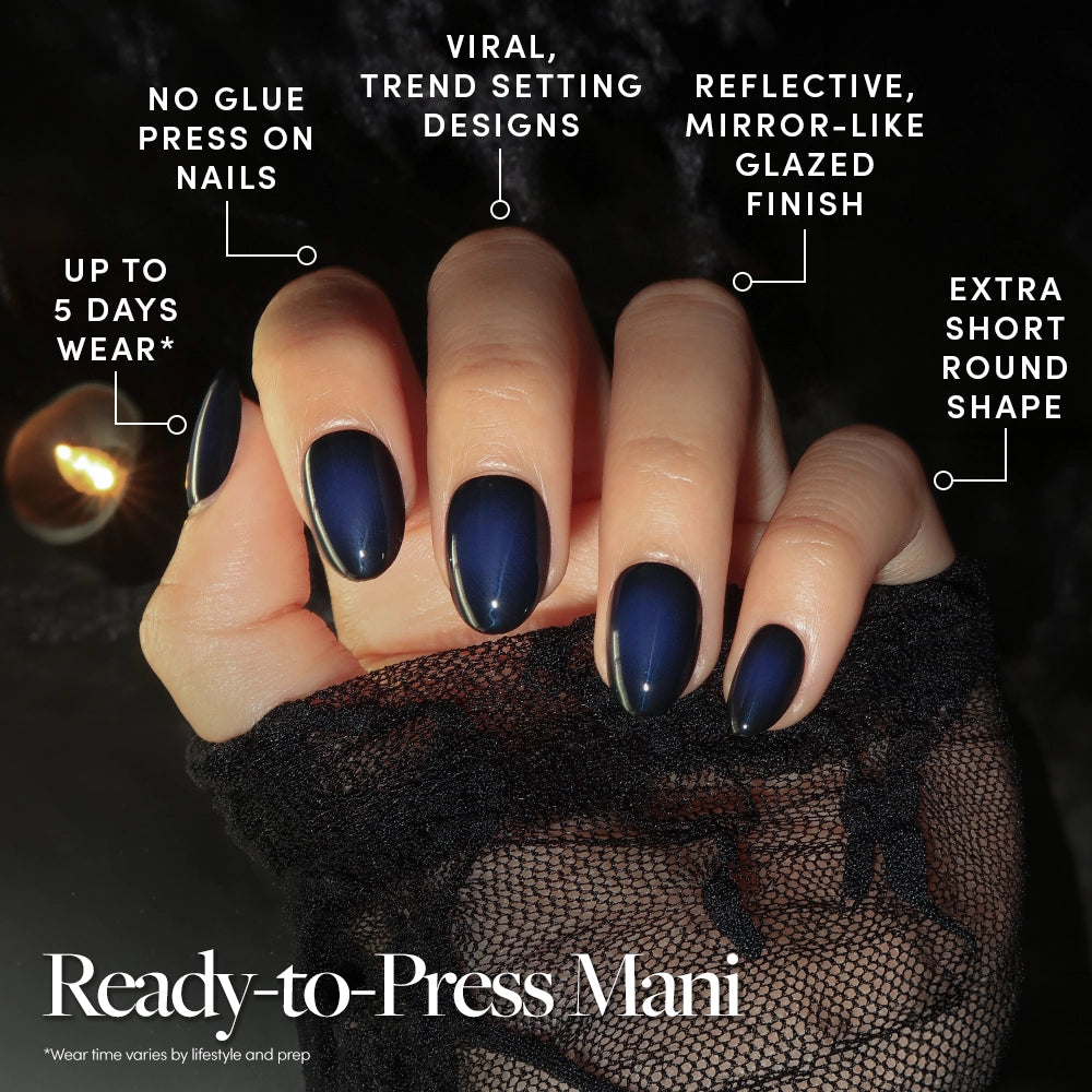 A hand with glossy, deep purple Purple Reign stick-on nails by glamnetic is shown, featuring a short round shape. Text highlights their no-glue design, viral popularity, reflective finish, and wear time of up to 5 days. A lacy sleeve covers the wrist. - Product image