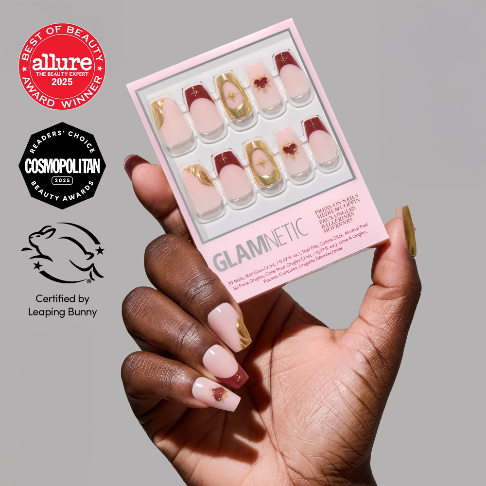 A hand with manicured coffin nails, featuring gold and pink 3D nail art, holds a box of glamnetic Queen of Hearts press-on nails. Award seals from Allure, Cosmopolitan, and Leaping Bunny appear on the left. - Product image