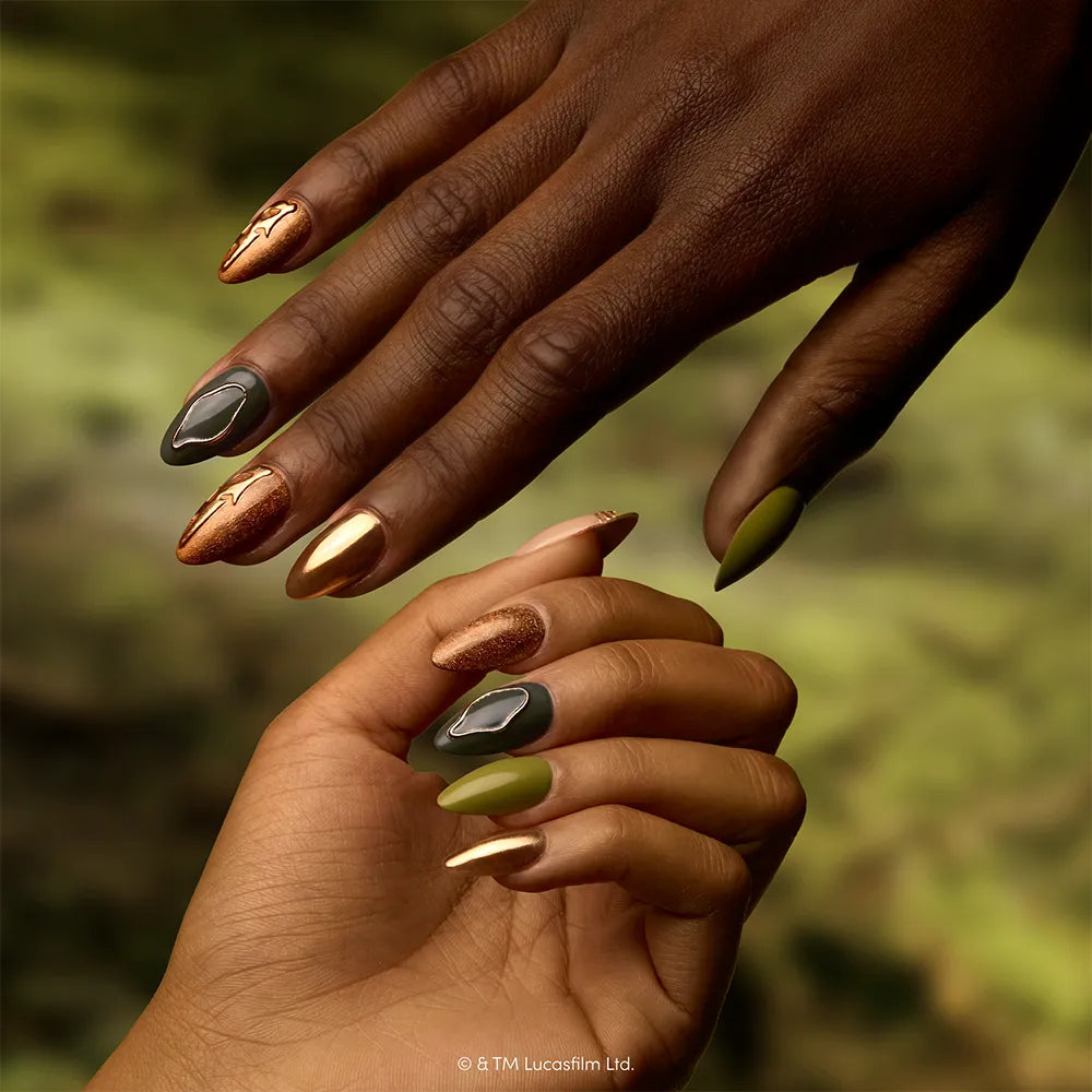 Rebellion - Two hands display the bold style of the glamnetic Rebellion press-on nail set, with long, pointed nails in metallic gold, matte green, and textured designs. One nail features a shiny black stone-like accent inspired by iconic STAR WARS press-ons. The softly blurred background glows in green tones.