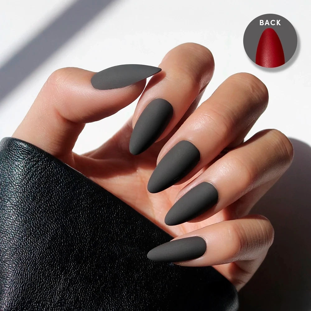 A hand with long, matte black stiletto press-ons from glamnetic’s Red Bottom set. A small circle shows the red undersides. The person wears a black leather sleeve.