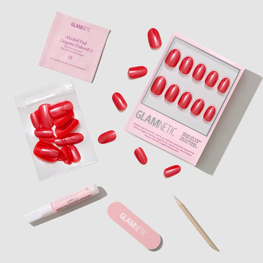 Glamnetic’s Red Confidence features salon-quality short round red press-on nails, plus an alcohol pad, nail glue, nail file, and cuticle stick—displayed on a light gray background with pink Glamnetic packaging.