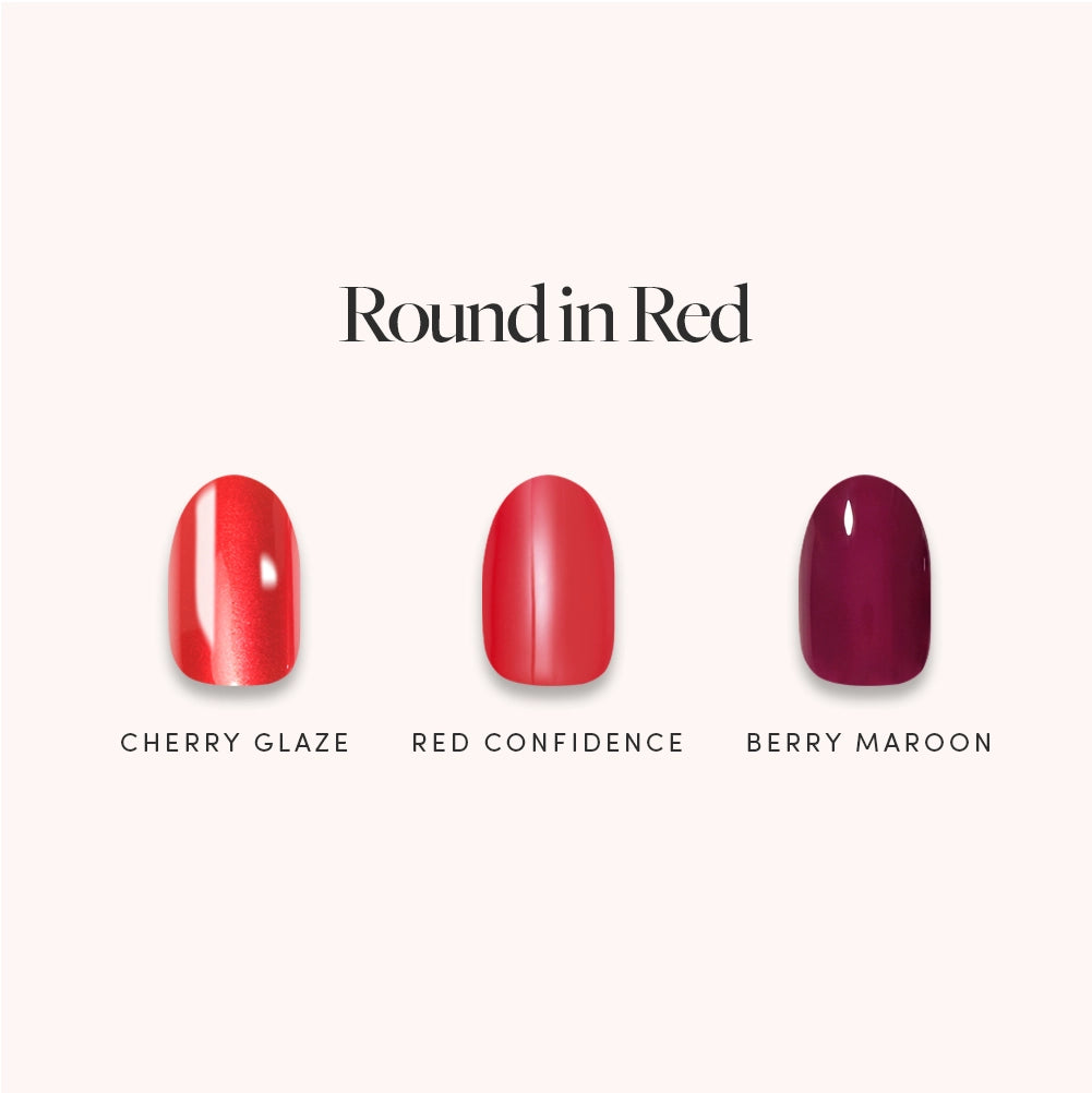 Three round nail polish swatches labeled Cherry Glaze (shimmery red), Red Confidence (classic red), and Berry Maroon (deep maroon) are displayed on a light background beneath the title "Round in Red" from glamnetic—offering perfect inspiration for salon-quality red press-on nails you can apply at home.
