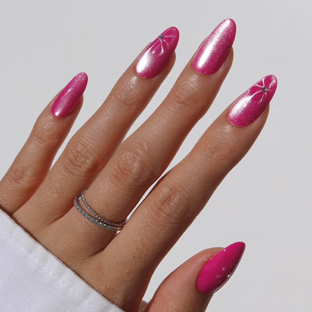 The hand features Rosy Siren nails by glamnetic—long, almond-shaped and shiny hot pink with minimal white line art on the middle and ring fingers. Two thin silver rings adorn the middle finger.