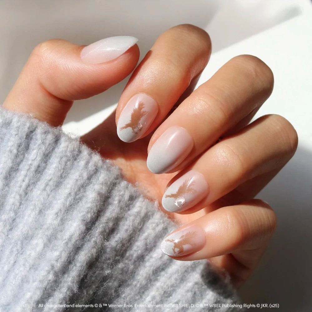 Rowena Ravenclaw™ short oval press-on nails with a sheer white ombre finish, featuring a bronze eagle emblem on two of the fingers.
