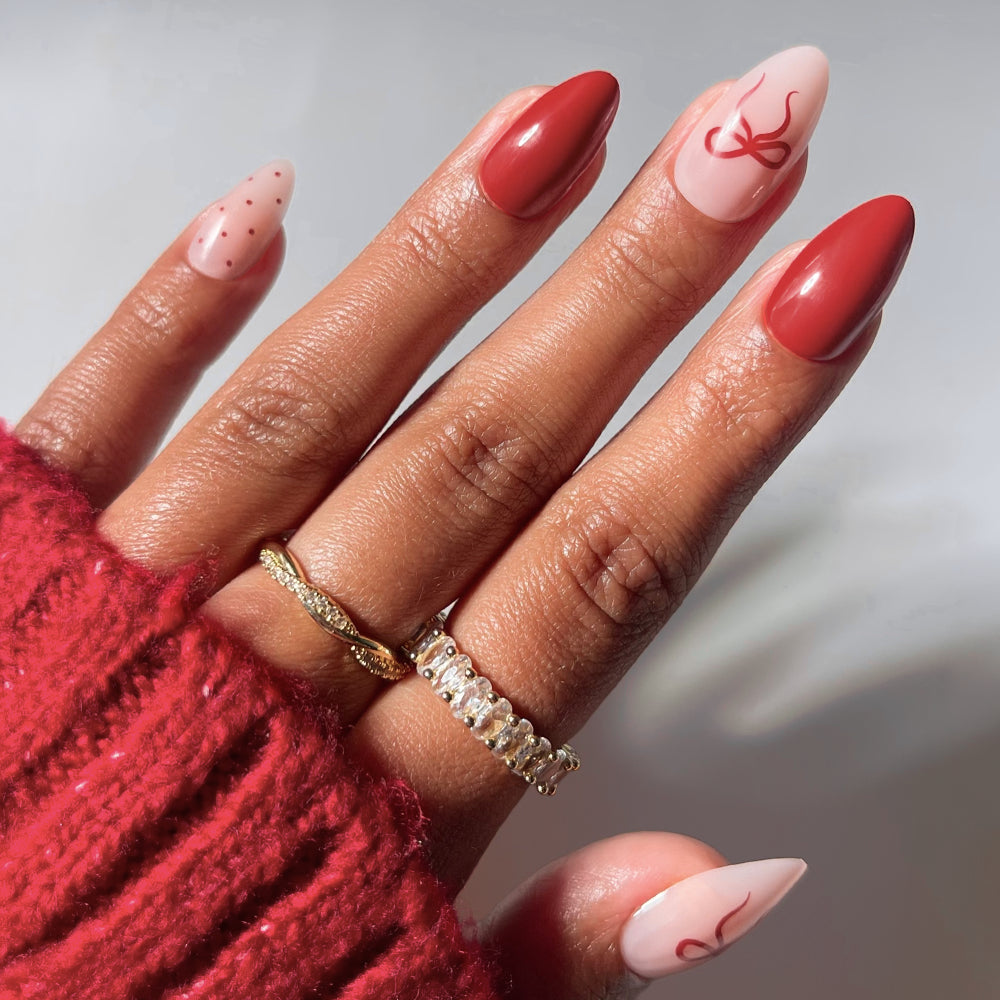 Royal Ribbons almond-shaped press-on nails featuring a holiday manicure of solid red polish, polka dots, and delicate red bow designs.