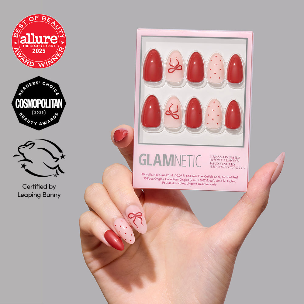Royal Ribbons - A hand holds a box of Glamnetic Royal Ribbons, featuring red and light pink almond press-on nails decorated with bows and polka dots, alongside Allure and Cosmopolitan award logos and a Leaping Bunny certification.