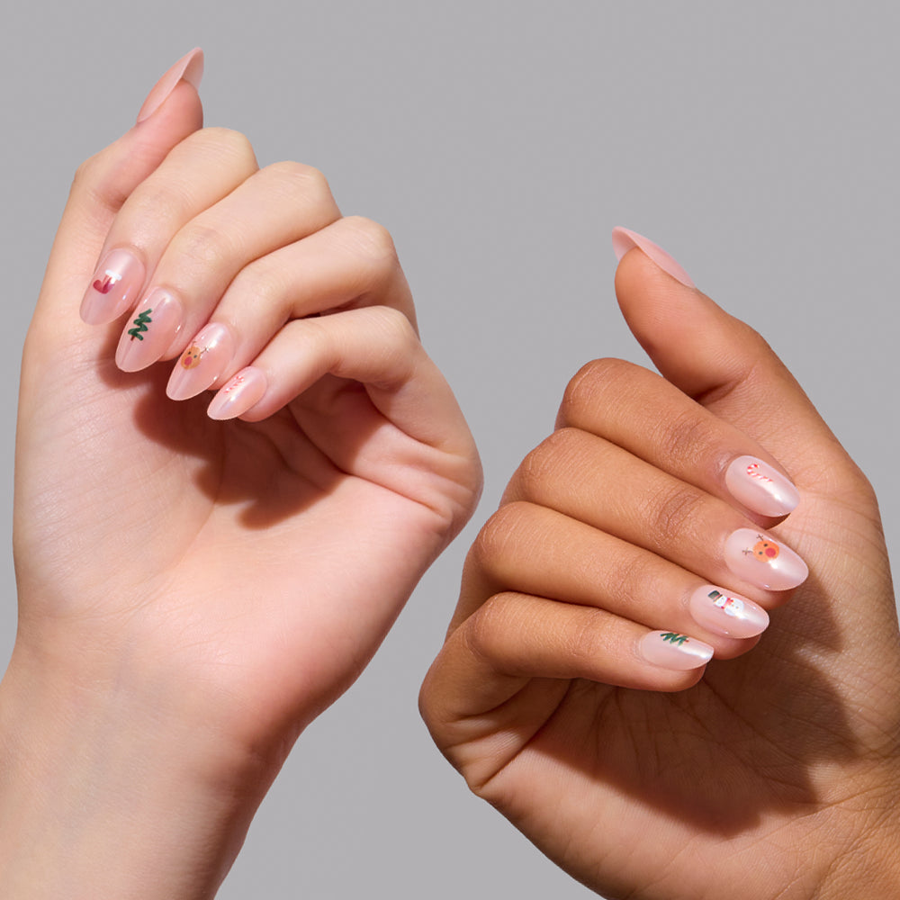 Santa's Babies - Glamnetic Santa’s Babies press-on nails featuring almond-shaped, sheer pink tips with small Christmas-themed decals including trees, reindeer, and candy canes.