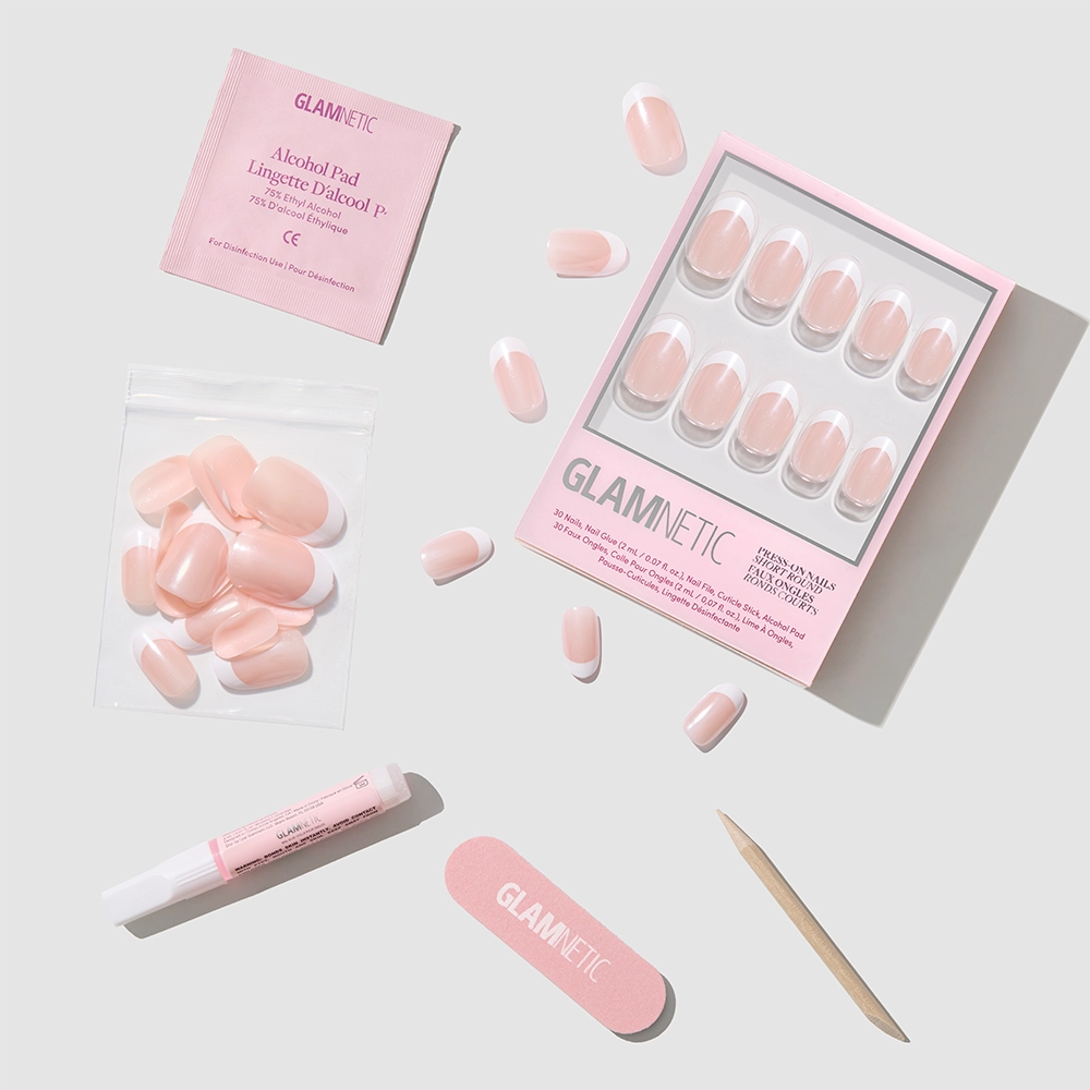 The glamnetic "She's a Pearl" set features pink press-on nails with a pearlescent glazed finish, plus alcohol pad, nail glue, adhesive tabs, nail file, and cuticle stick—all displayed on a light gray background. - Product image