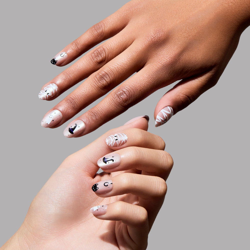 Two hands with light and medium skin tones display the glamnetic Shriek Boutique almond-shaped press-on nails, featuring white nails adorned with black abstract designs, lines, and dots, set against a plain gray background. - Product image